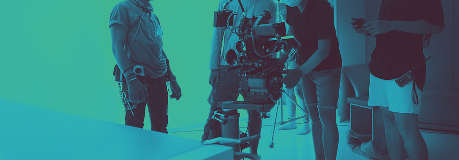 Three people working on a video production set with a large camera on a tripod, green screen background