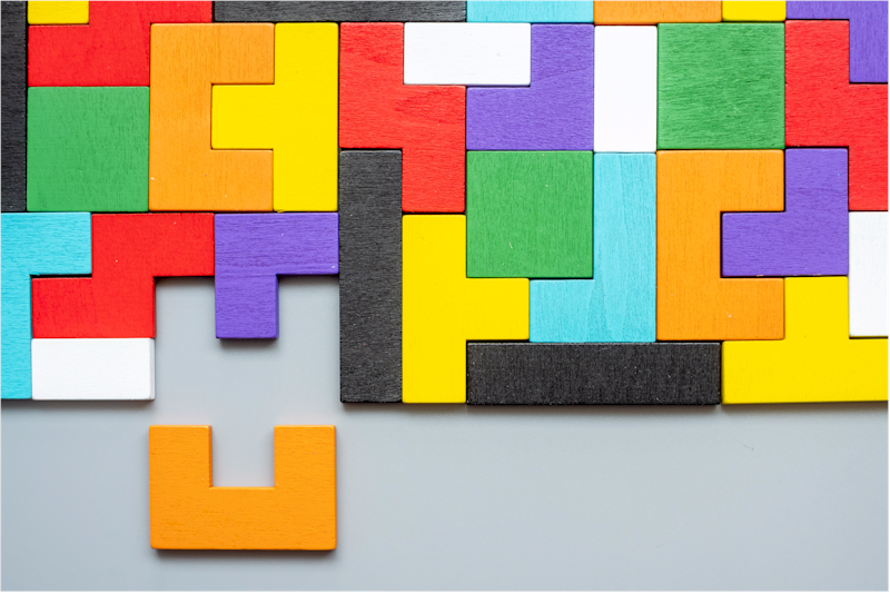 A colourful wooden tangram puzzle with many pieces fitted together and one orange piece separate