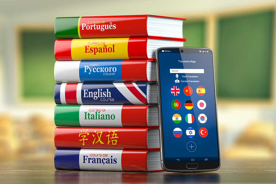 A stack of language textbooks next to a smartphone displaying a translation app with various country flags.
