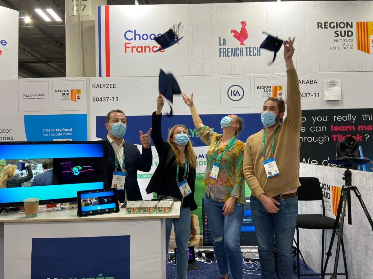 Four people in face masks throwing graduation caps in the air at a trade show booth