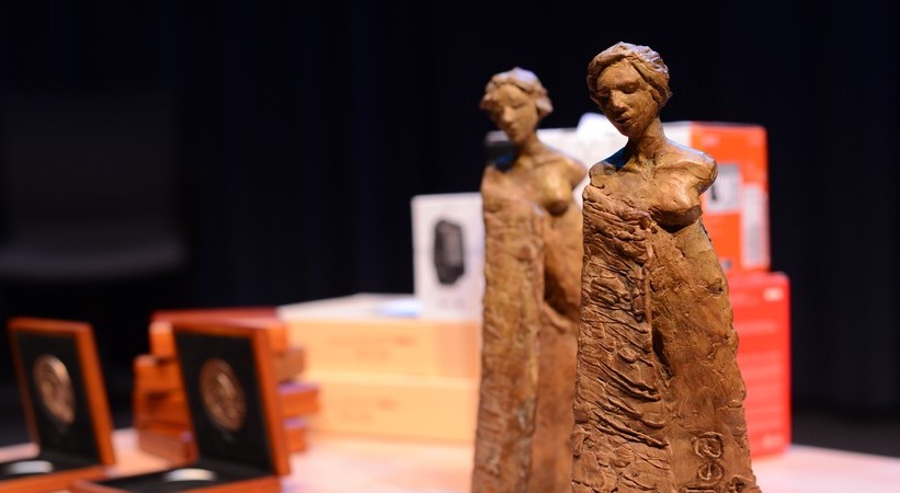 Two bronze statuettes and several award boxes on a table, with a dark background