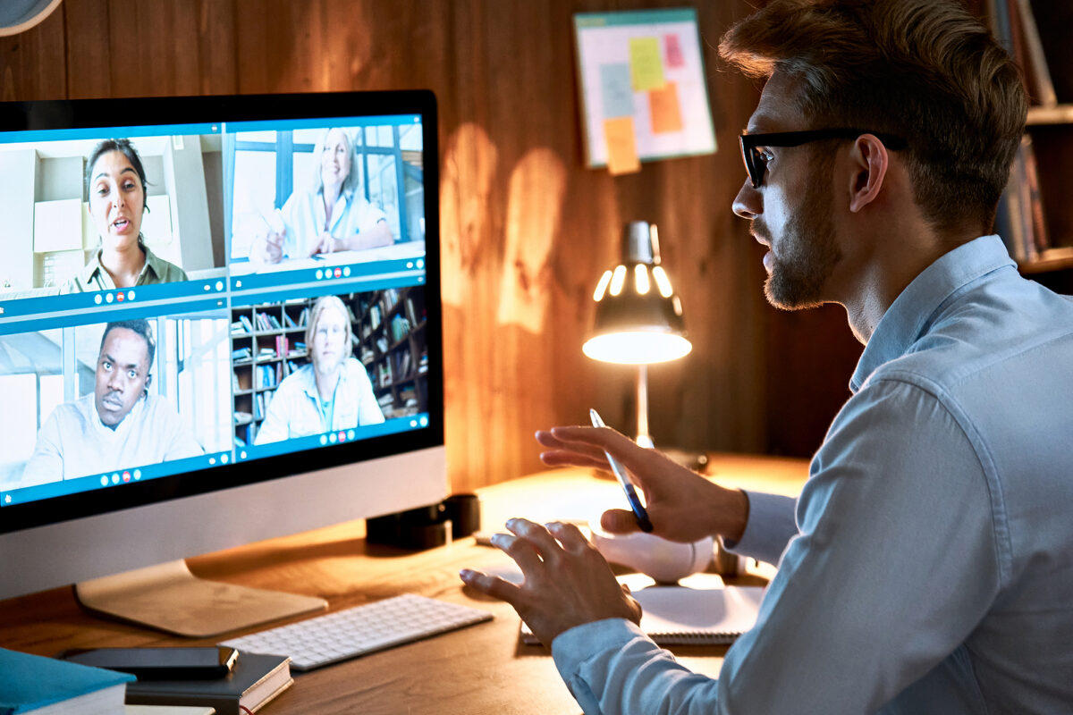 Man in glasses on a video call with four other people, gesturing with a pen in his hand.