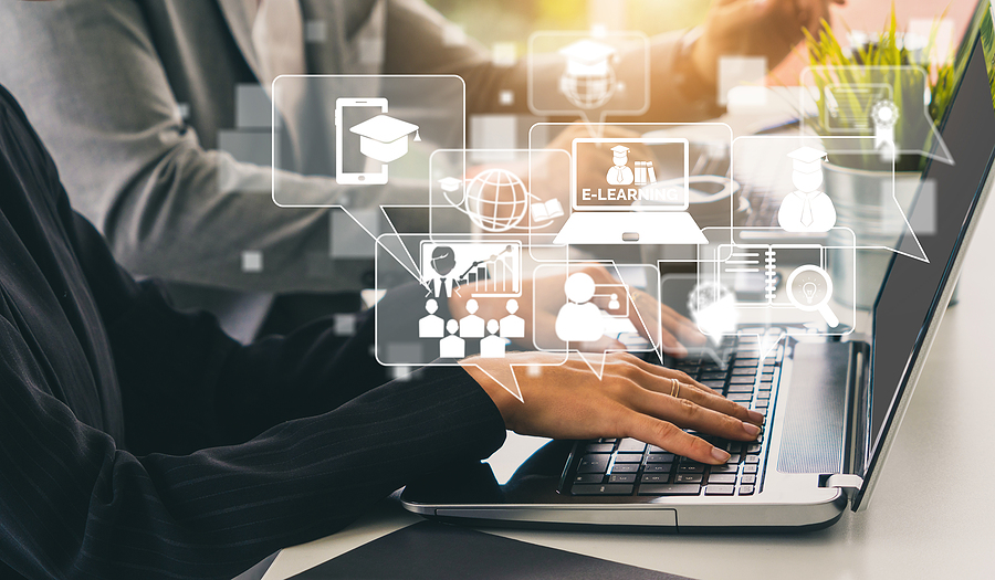Hands typing on a laptop keyboard with various e-learning icons floating above, including a graduation cap, globe, and
