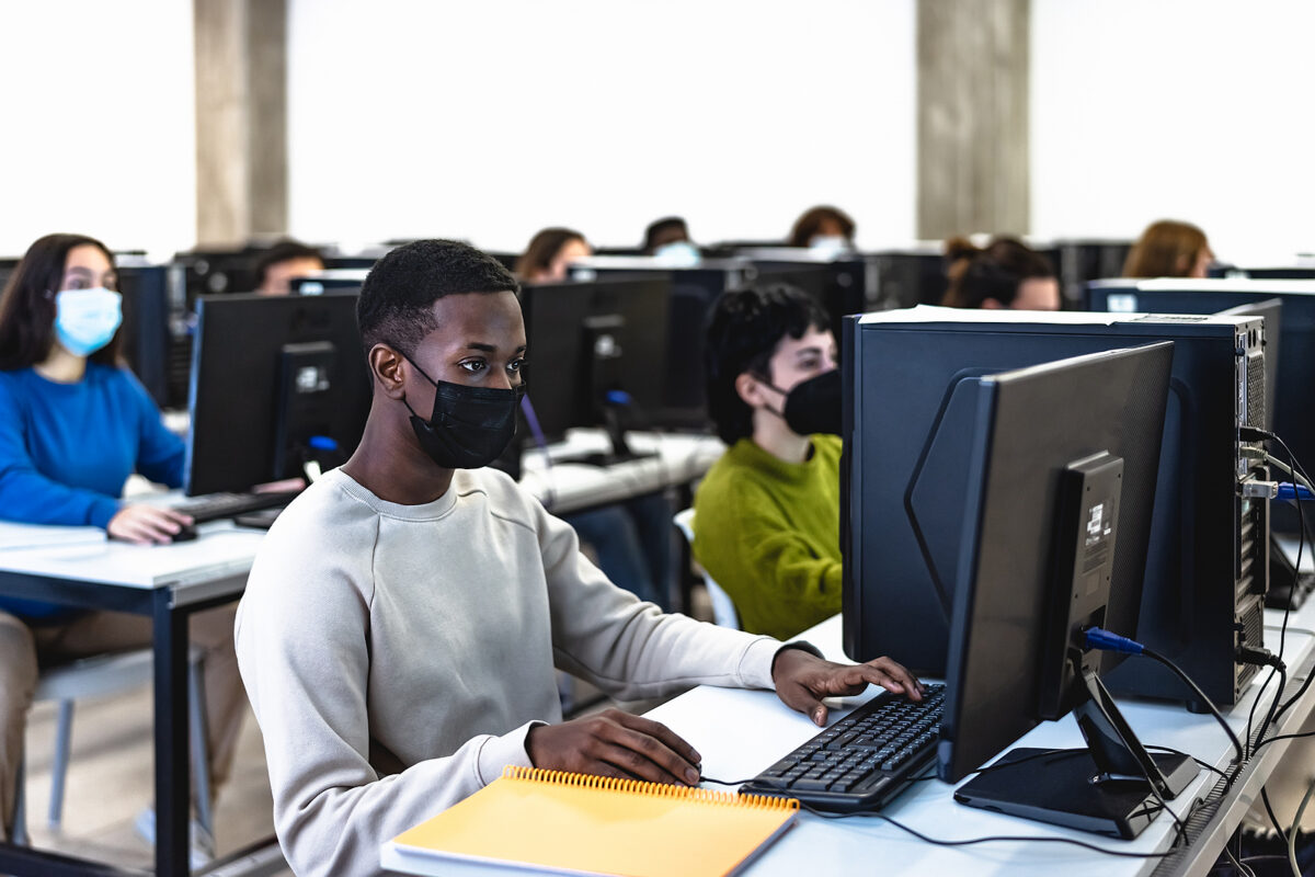 Young students wearing face masks working on computers in a classroom or computer lab.