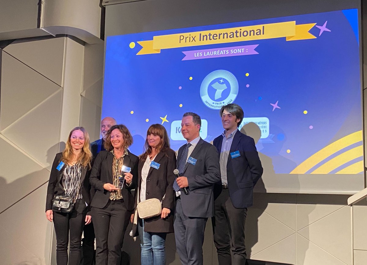 Six people on stage, with a screen behind them showing "Prix International" and a logo.