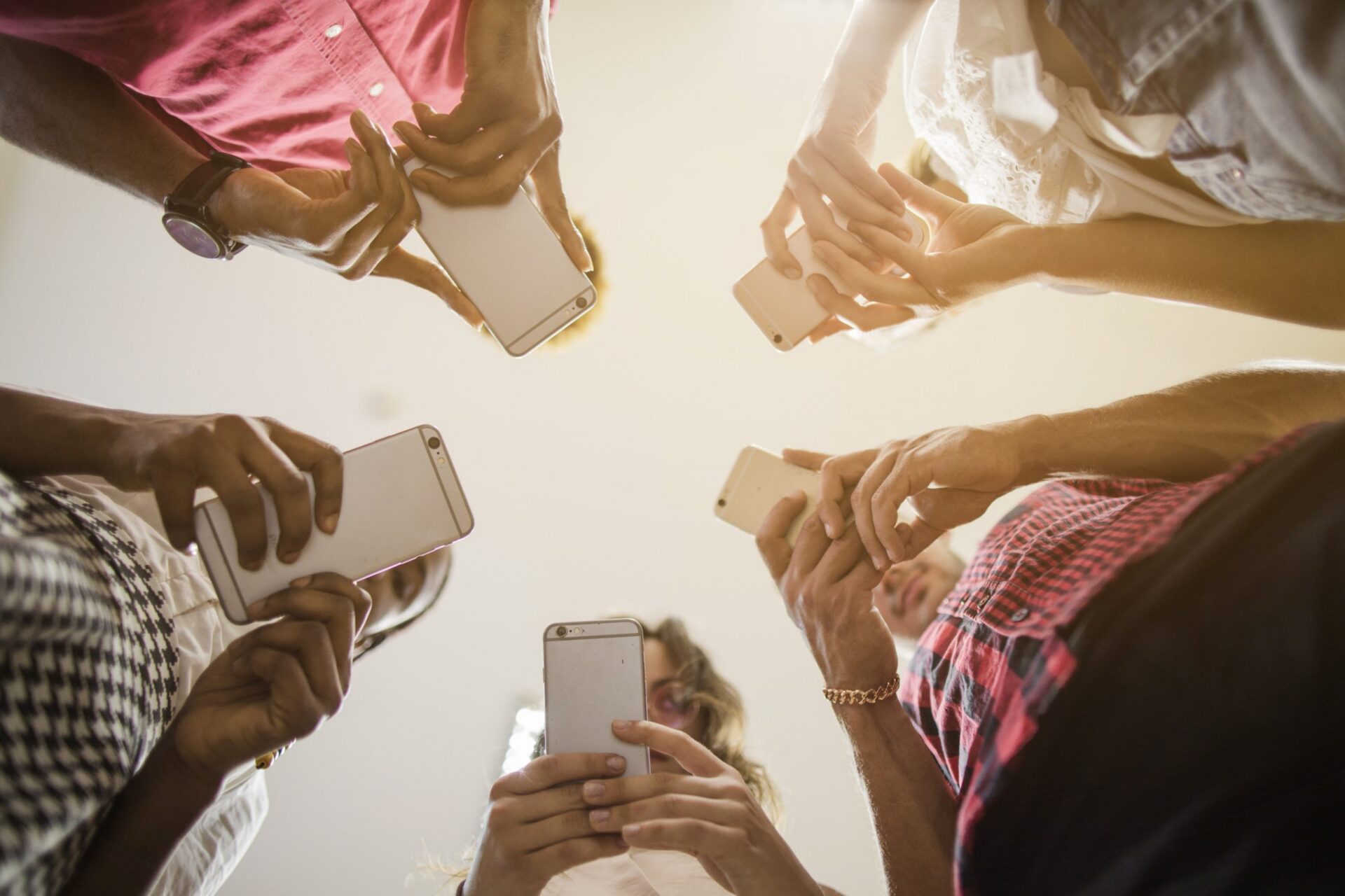 Five people holding smartphones in a circle, viewed from below, against a bright sky.