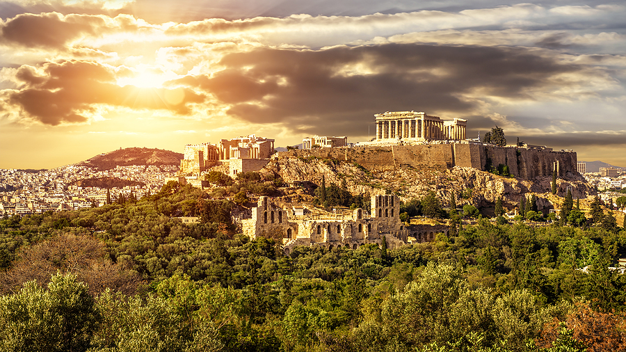 The Acropolis of Athens at sunset, with the Parthenon and other ancient ruins atop a hill.