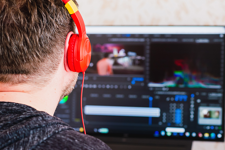 Person wearing red headphones, looking at a computer screen displaying video editing software.