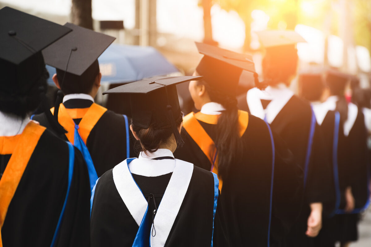 Rear view of graduates in caps and gowns walking in a line, with a bright light in the background