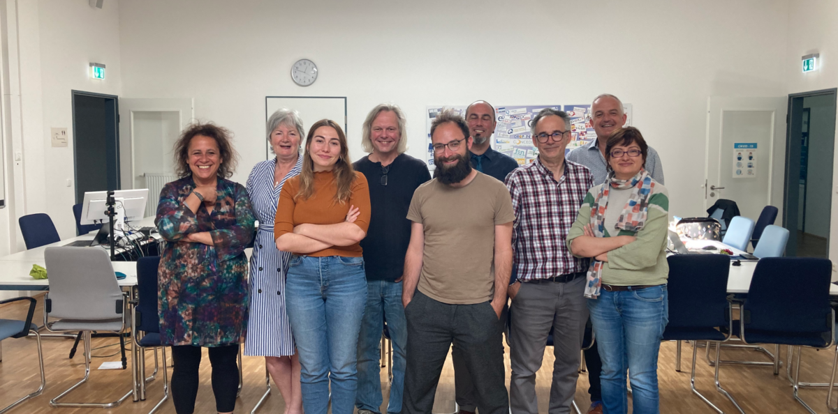 Group photo of ten people, five men and five women, standing and smiling in a bright room.