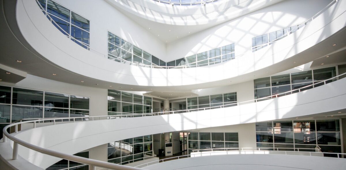 A modern, multi-level building interior with white curved walls, large windows, and a glass ceiling.