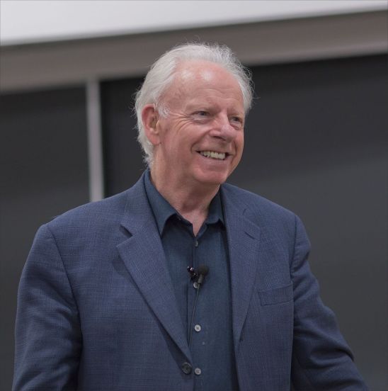 Tony smiling, wearing a blue shirt and jacket, with a small microphone clipped to his shirt.