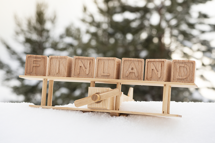 Wooden toy plane on snow with wooden blocks spelling FINLAND on its wings, blurred trees in background.