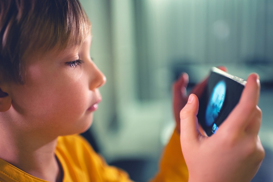 Close-up of a young boy in a yellow top, looking intently at a smartphone held in his hands.
