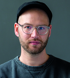 Jonathan Stauffer, a man with a beard, glasses and a black cap, looks directly at the camera.