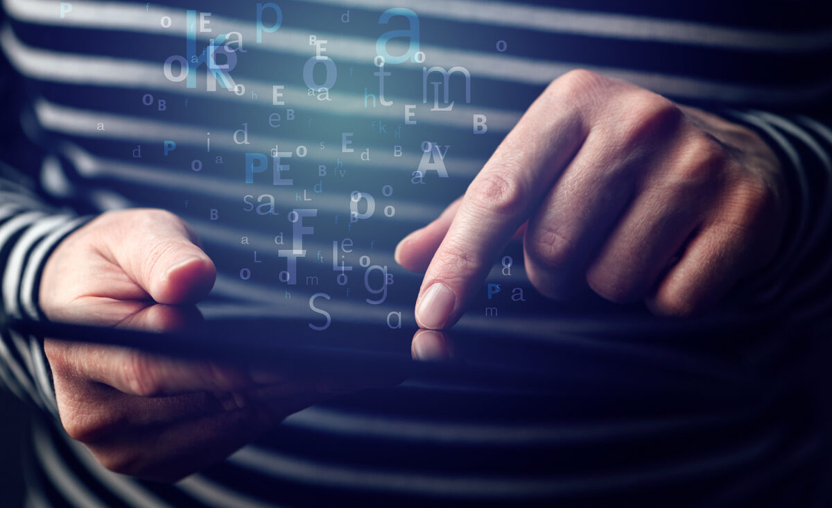 A person's hands interacting with a tablet, with letters and symbols floating above the screen.