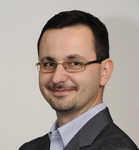 Headshot of Igor, a man with short dark hair, glasses and a moustache, smiling at the camera