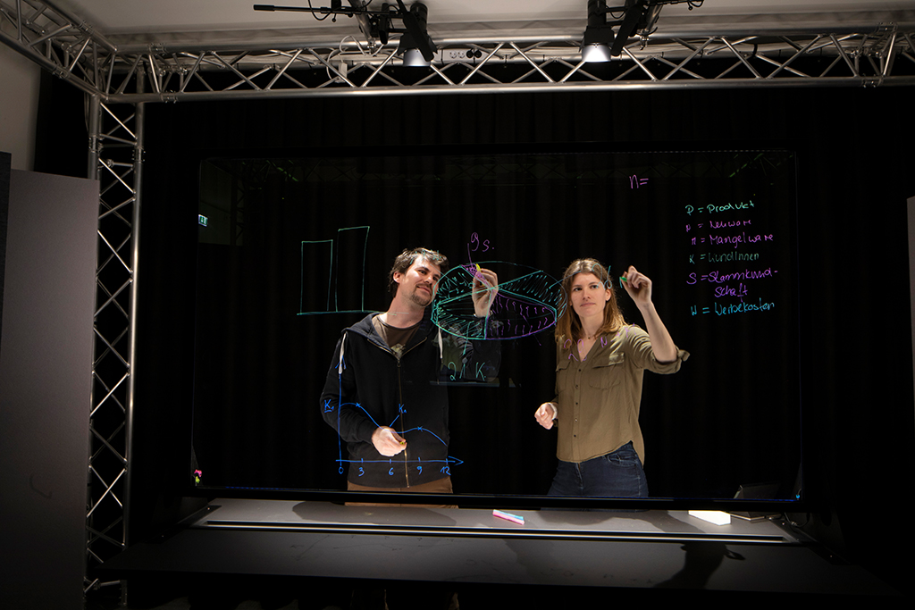 Two people, a man and a woman, writing and drawing graphs on a transparent screen in a dark room.