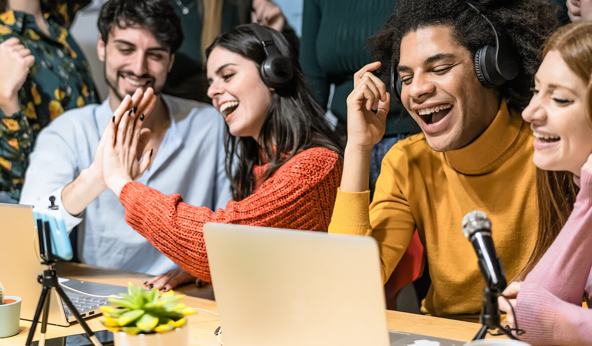 Four young adults, two men and two women, laughing and high-fiving while recording a podcast.