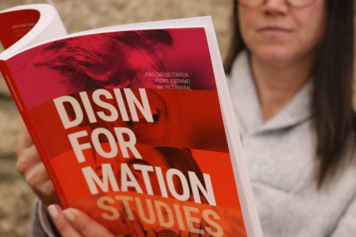 A person holding an open book titled Disinformation Studies, with authors João Carlos Correia, Pedro Jerónimo, Inês Amaral