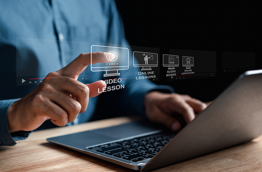 A person's hand touching a holographic screen displaying 'Video Lesson' and other online learning options.