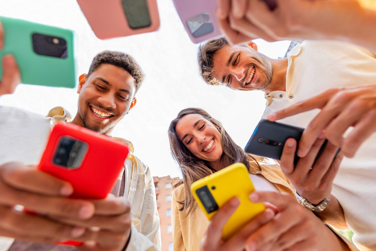 Low-angle view of five young people looking down at their smartphones, smiling and laughing.