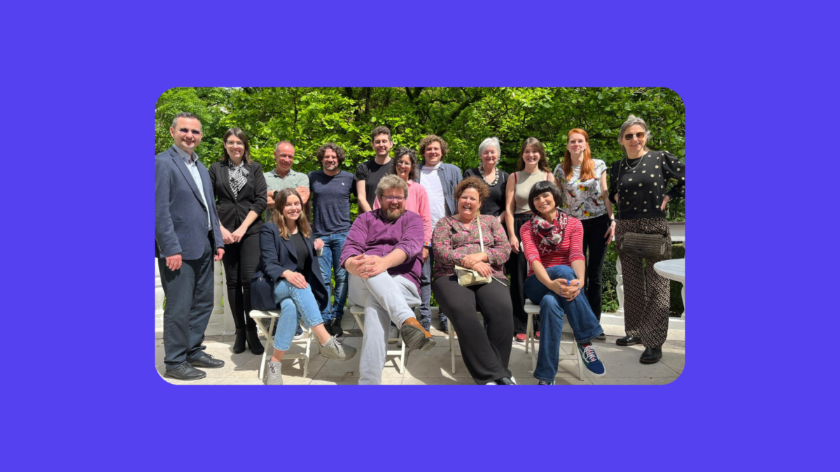 Group photo of 17 people, some standing, some sitting, outdoors in front of green trees.