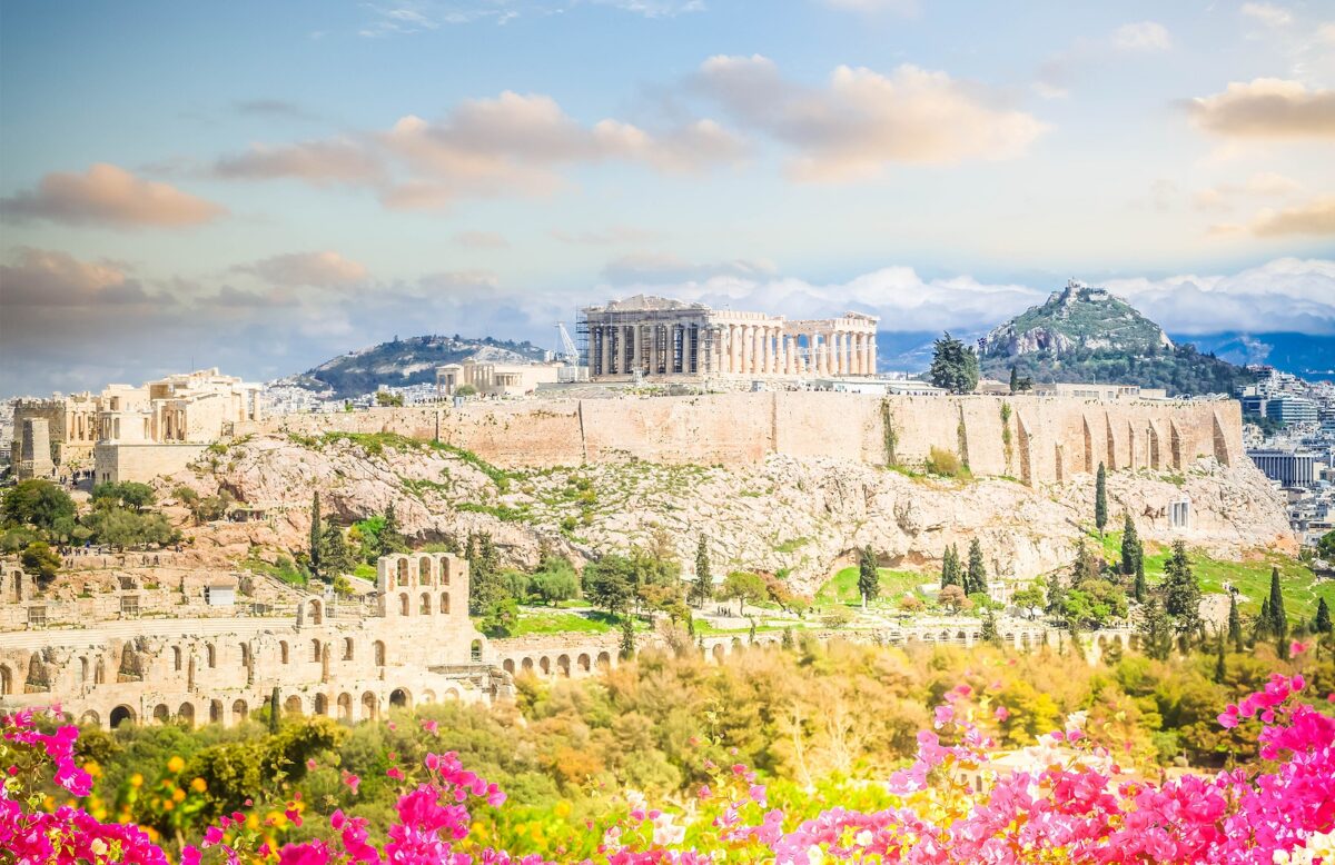 Panoramic view of Athens with the Parthenon on the Acropolis, surrounded by ancient ruins and pink flowers.