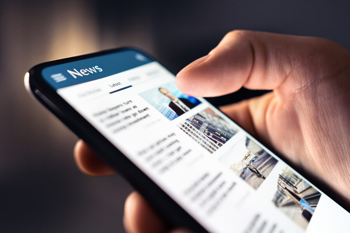 A person's hand holding a smartphone displaying a news app with the word "News" at the top.