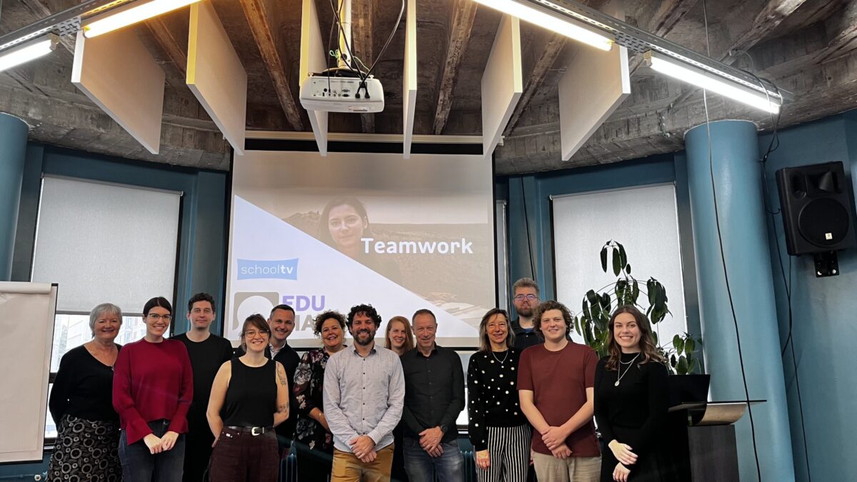 Group photo of 14 people smiling at the camera, standing in front of a screen displaying "Teamwork".