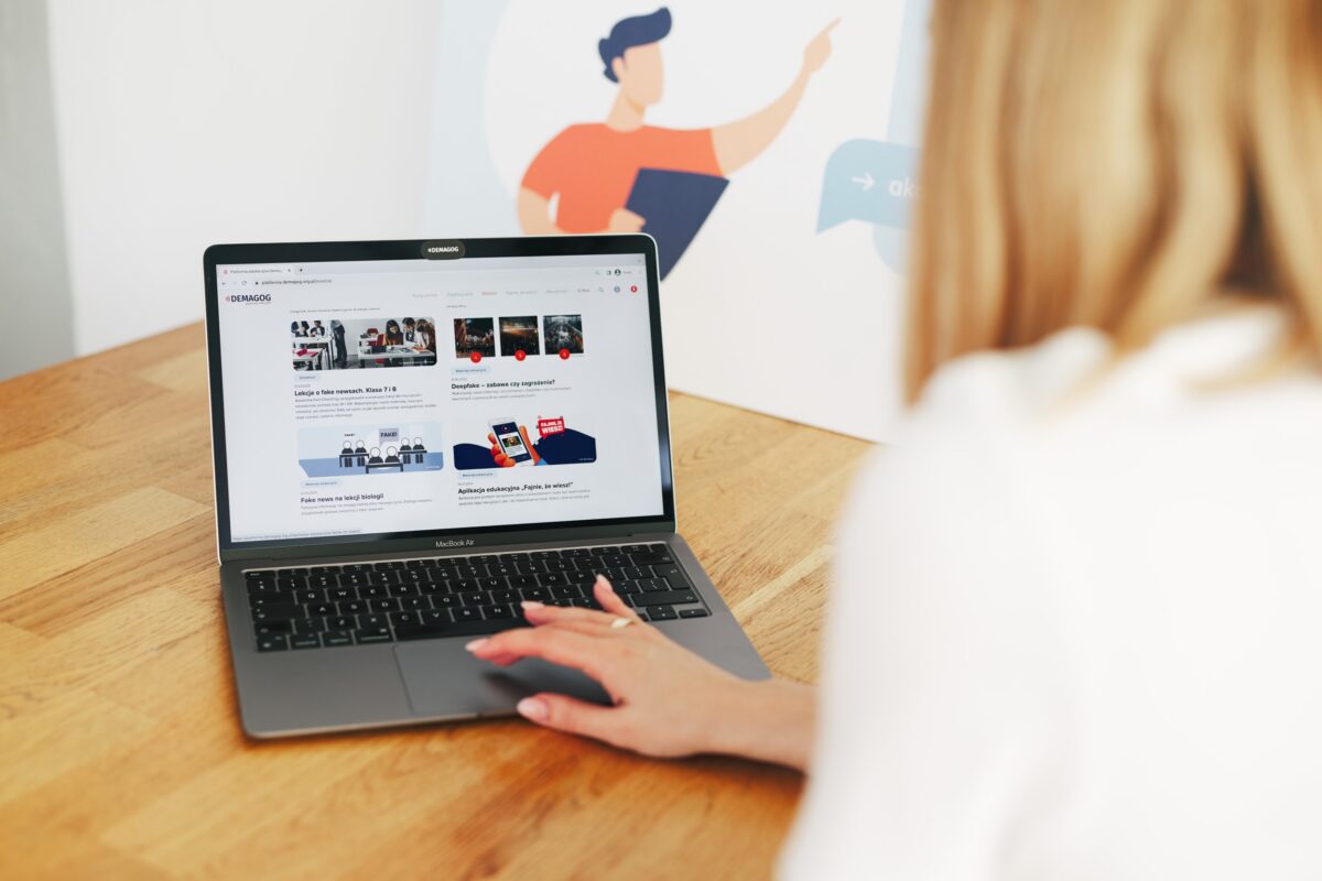 A person's hands on a laptop keyboard, displaying the Demagog website with articles and images.
