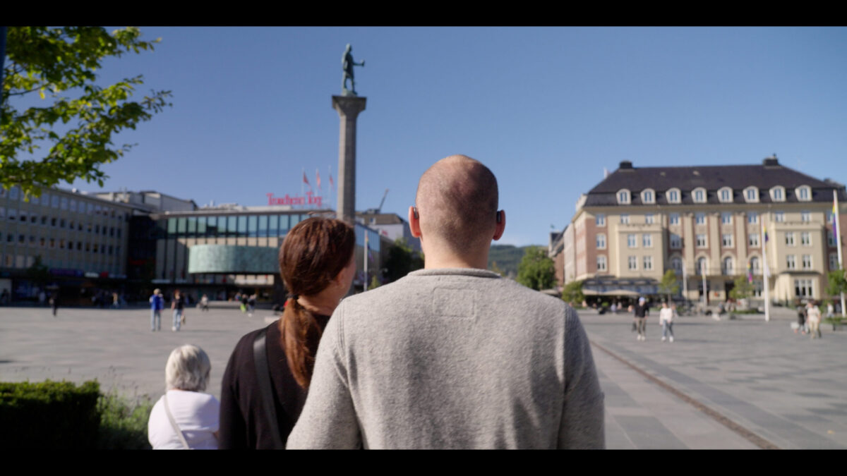 Two people from behind, looking at a city square with a statue on a column and buildings.