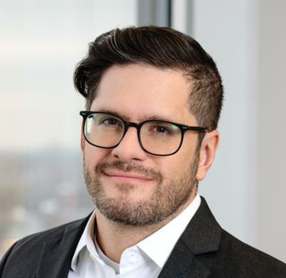 Headshot of Landry, a man with dark hair, glasses, and a beard, wearing a suit jacket and white shirt