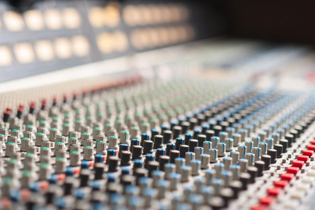 Close-up of an audio sound mixer with rows of grey, black, blue, green, and red buttons and knobs