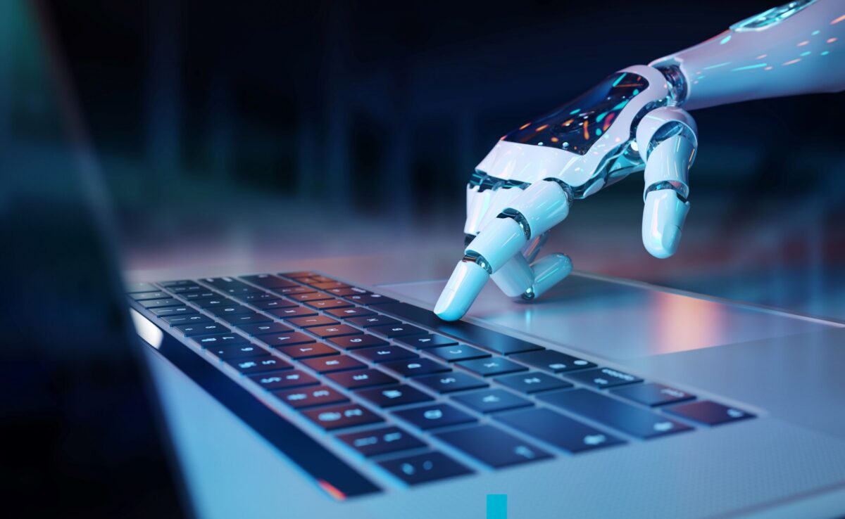 A white robotic hand with blue glowing accents presses a key on a silver laptop keyboard.