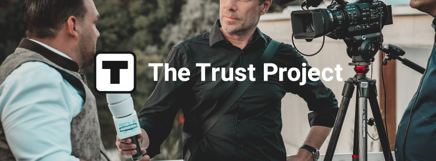 A reporter holding a microphone with The Trust Project logo and text, interviewing a man.
