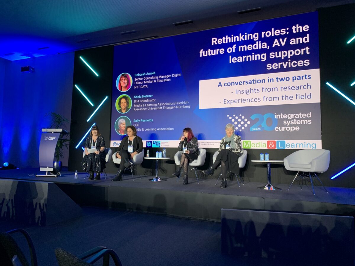 Four women on a stage at a conference, with a large screen behind them displaying the title "Rethinking roles: the future