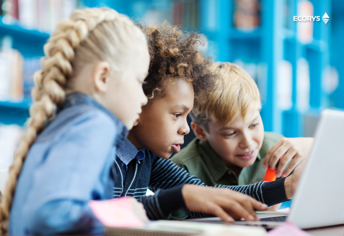 Three primary school children, two boys and a girl, looking at a laptop screen together.