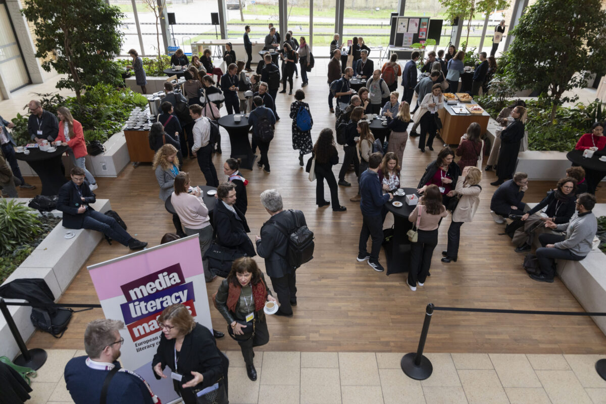 High-angle view of a crowded conference hall with people networking and a Media Literacy Matters banner