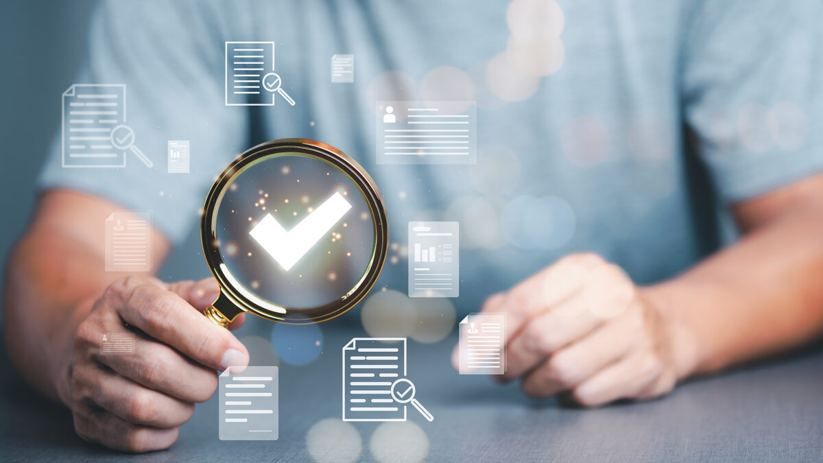 A person holds a magnifying glass over a glowing white tick mark, surrounded by document icons.