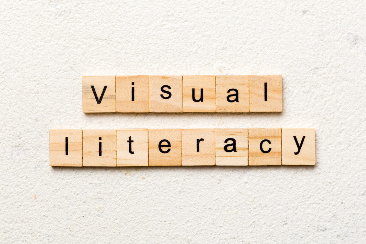 The words "visual literacy" spelled out in black letters on two rows of wooden scrabble tiles.