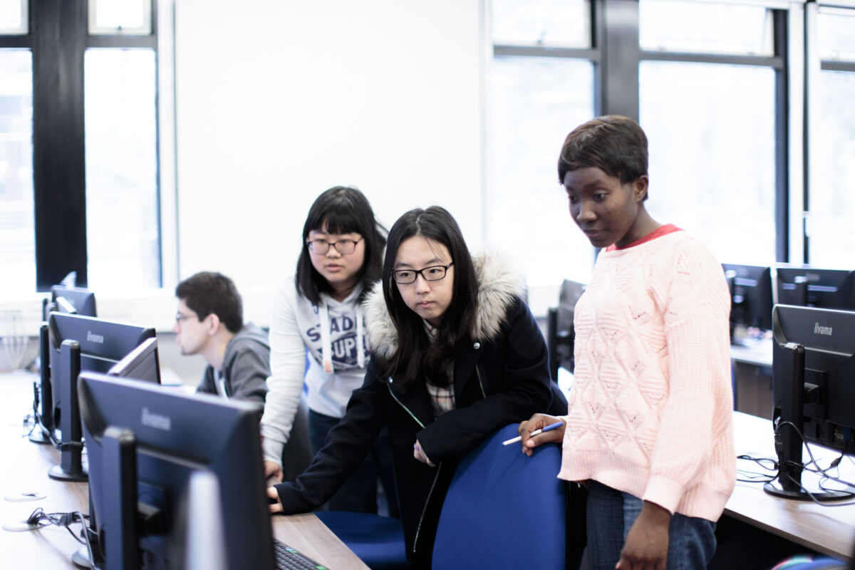 Three students, two East Asian and one Black, look at a computer screen in a university computer lab.