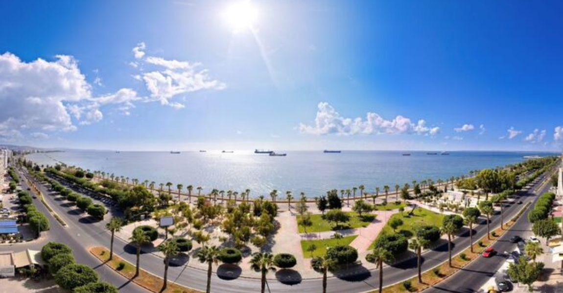 Panoramic view of Limassol, Cyprus, showing a sunny coastline with a road, palm trees, and the sea.