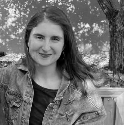 Megan Mallia, a young woman with long hair, smiling and wearing a denim jacket, outdoors.