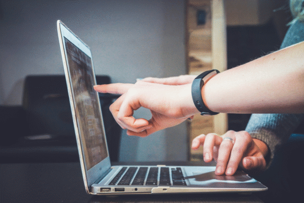 A person pointing at a laptop screen, while another person types on the keyboard.