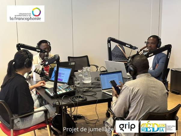Four people with headphones and microphones record a podcast, with laptops and equipment on a table.
