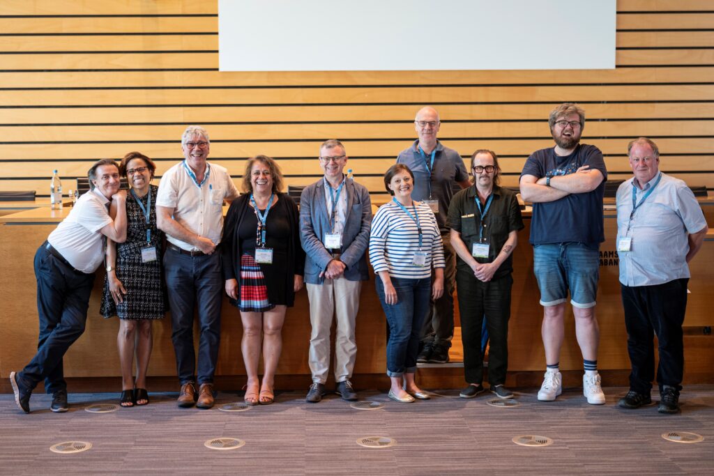 The Media & Learning Management Board: 11 people, 4 women and 7 men, standing in a line and smiling.