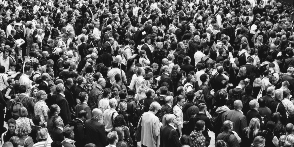 A high-angle, black and white shot of a dense crowd of people, mostly seen from behind.