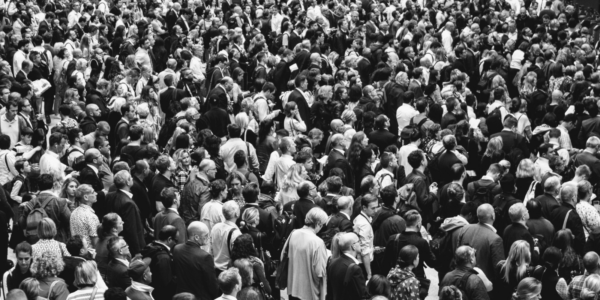 A high-angle, black and white shot of a dense crowd of people, mostly seen from behind.