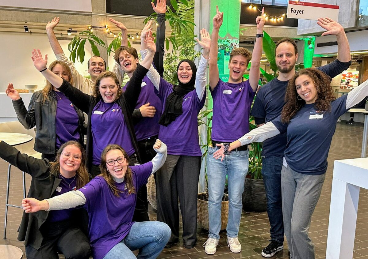 Group of 12 students and staff, some with arms raised, smiling at the camera in an indoor setting.